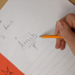 En barnhand skriver ordet Åmch på ett papper
